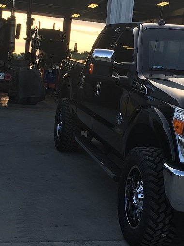 black truck in front of service bay with semi-truck on lift